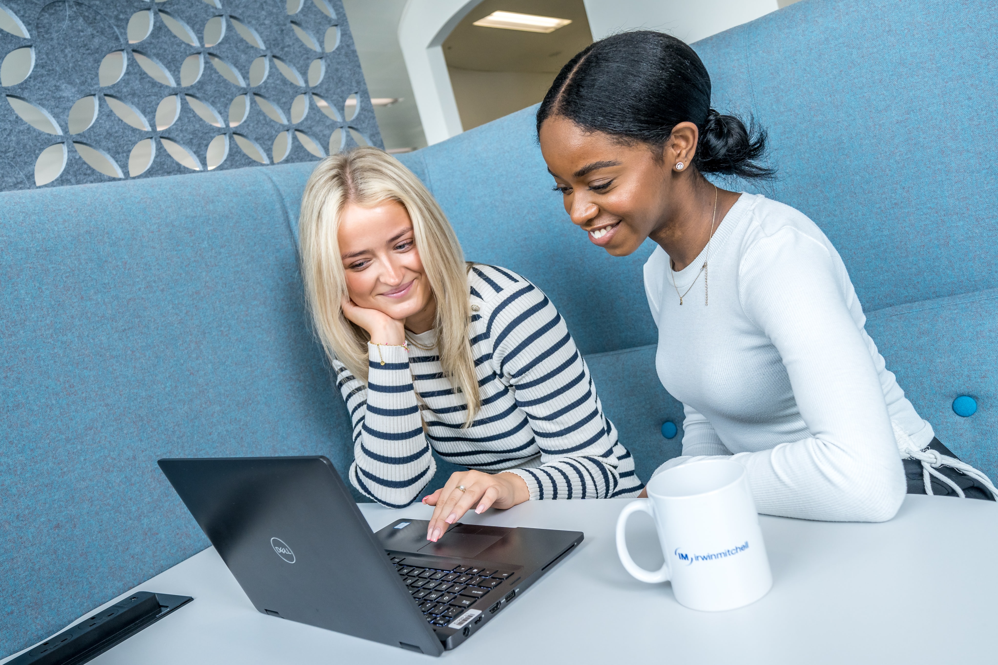 Two apprentices sat in a booth in an office, working together at a laptop